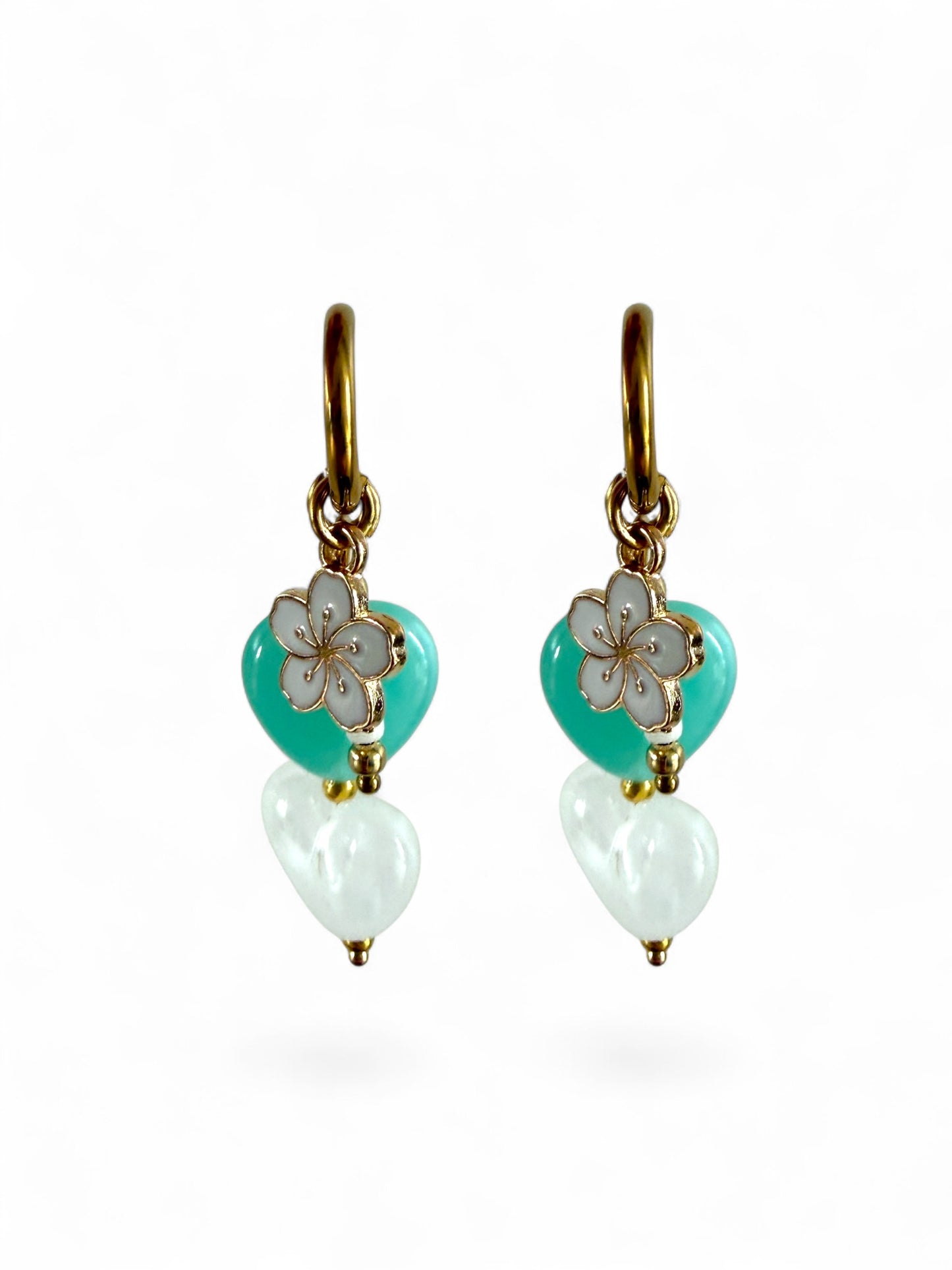 De Lagoon oorbellen zijn gouden stainless steel oorbellen met een wit en turquoise hartje, een wit bloemen bedeltje en witte kralen 
