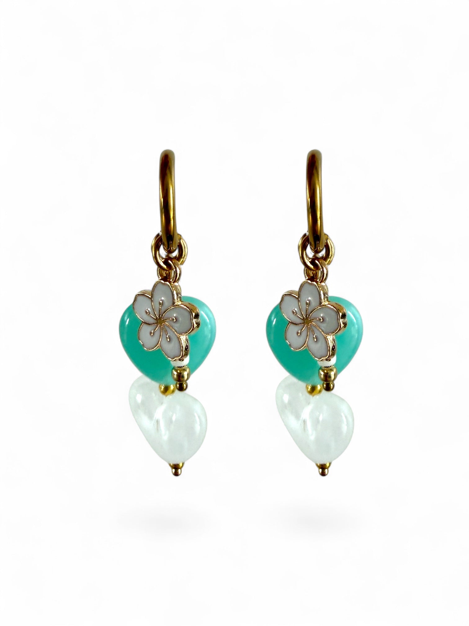 De Lagoon oorbellen zijn gouden stainless steel oorbellen met een wit en turquoise hartje, een wit bloemen bedeltje en witte kralen 