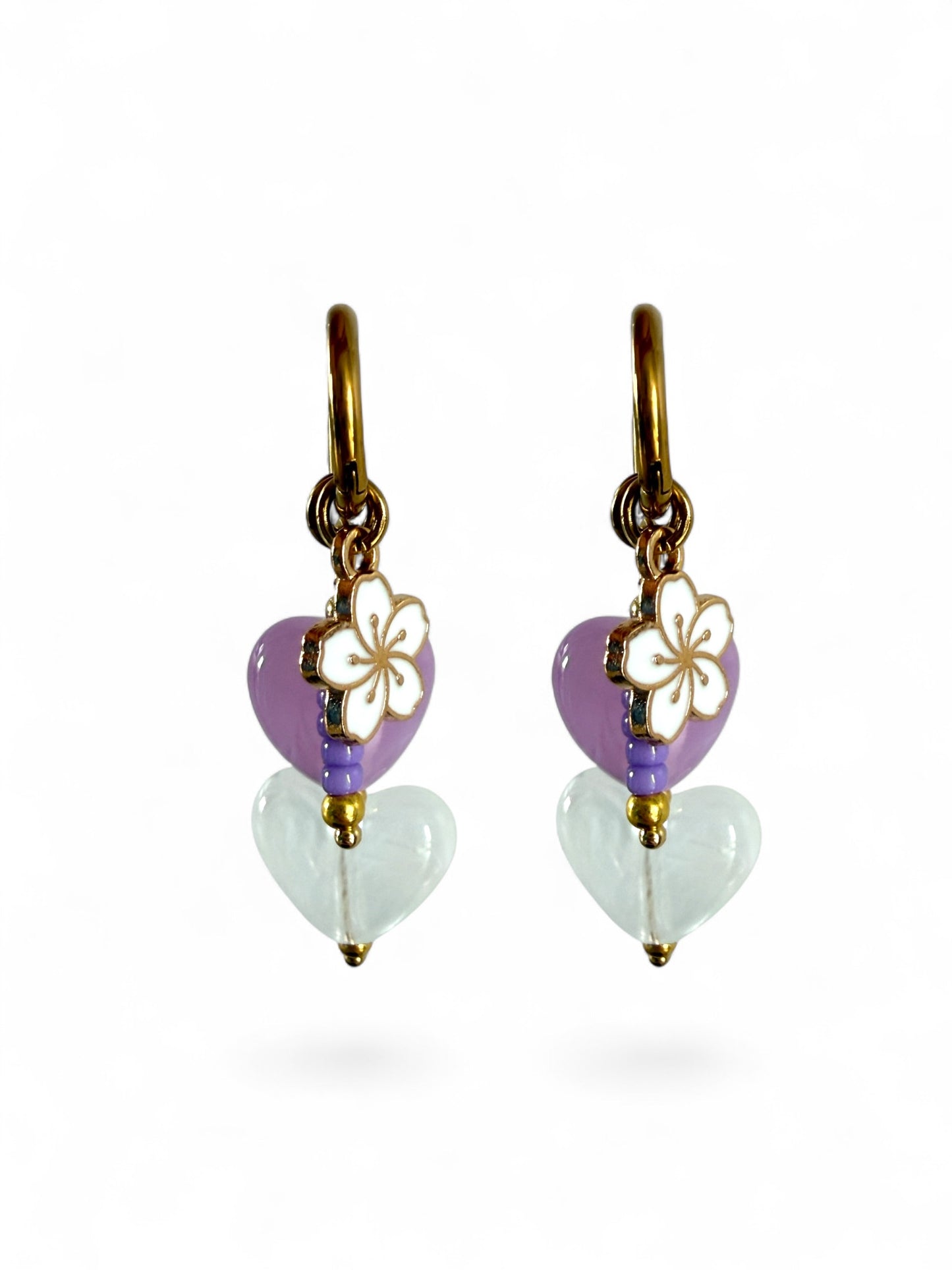 De lavender oorbellen zijn gouden stainless steel oorbellen met een wit en paars hartje, een wit bloemen bedeltje en paarse kralen 