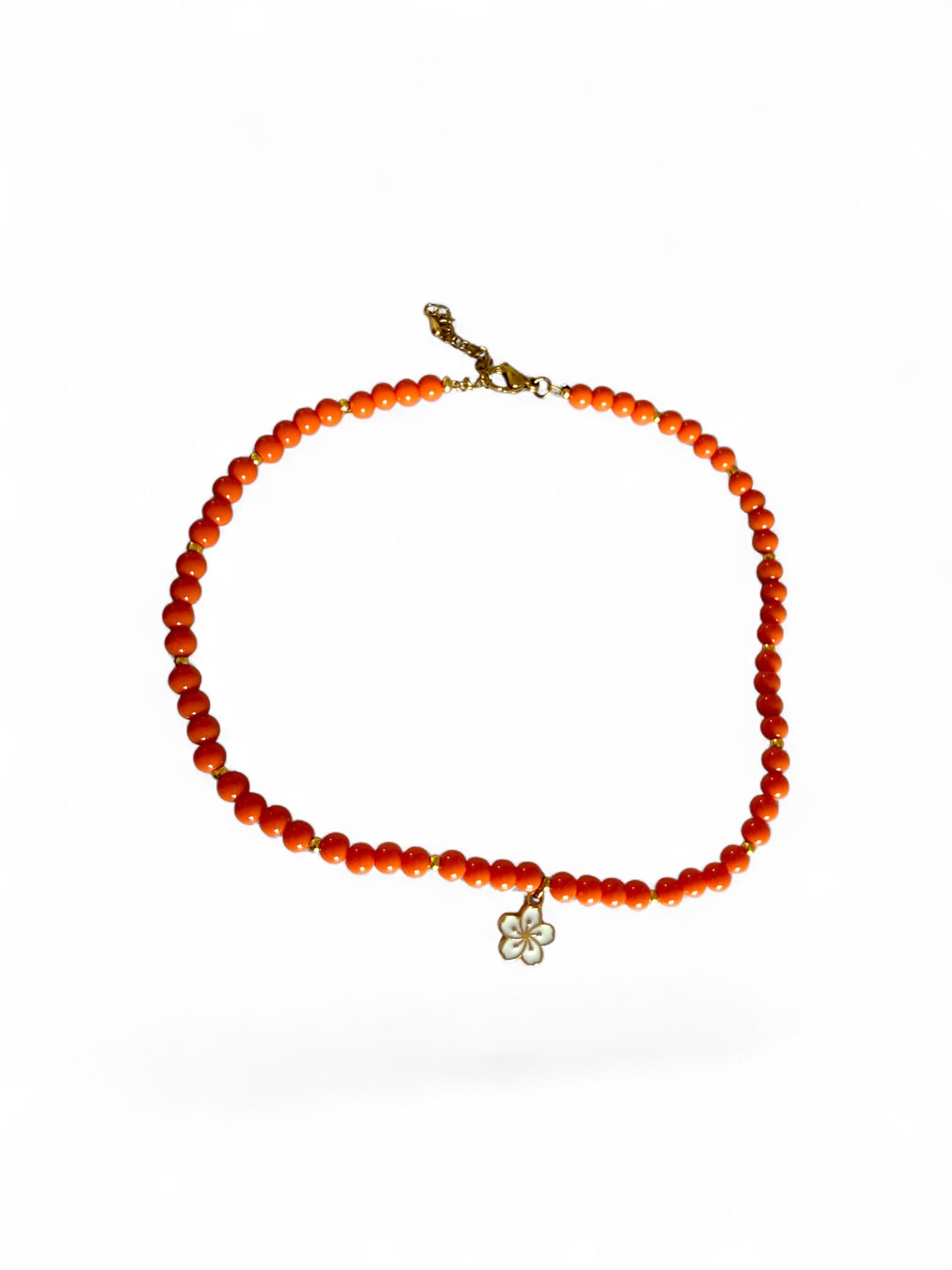 Sandie ketting is met oranje kralen handgemaakt met een witte bloemenbedel
