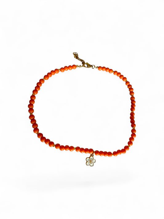 Sandie ketting is met oranje kralen handgemaakt met een witte bloemenbedel
